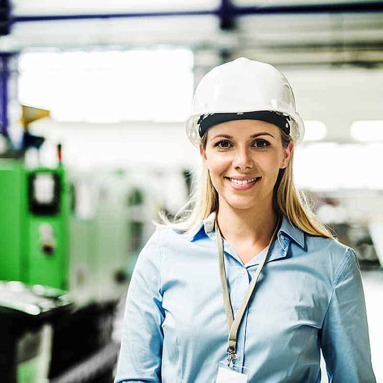 female health and safety officer wearing hard hat on engineering shop floor square format